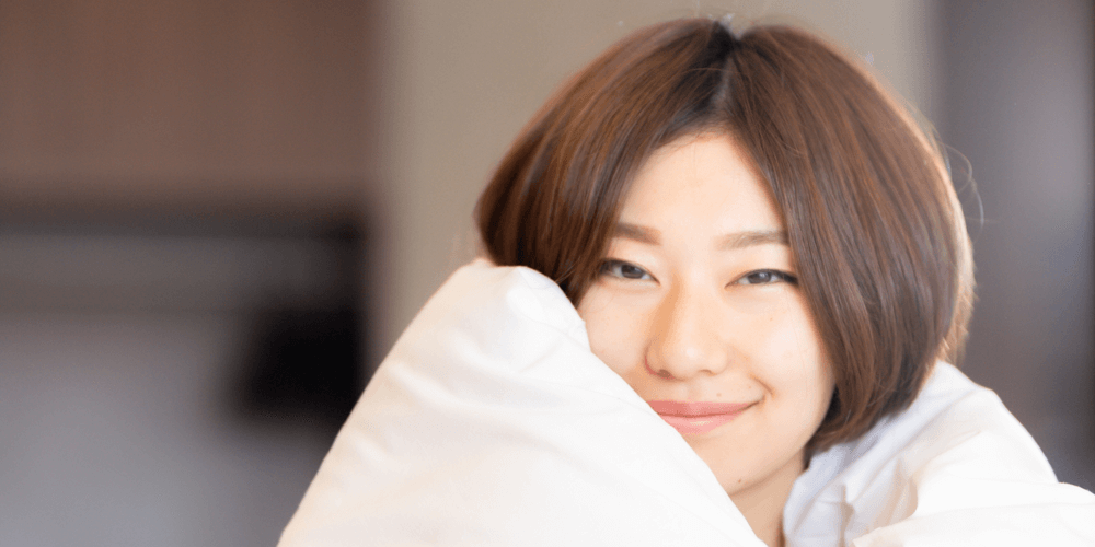 布団を羽織る笑顔の20代女性